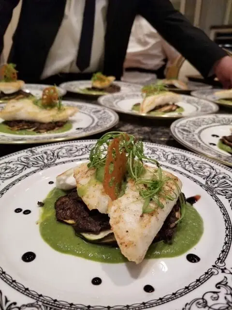 Gourmet plated white fish with green puree and microgreens served in fine dining setting with professional chef service